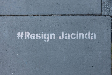 Stencilled lettering on a New Zealand pavement says '#Resign Jacinda' . Political statement slogan.Hashtag
