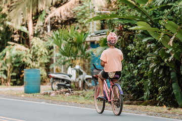 Fototapeta premium Imagen horizontal desde atrás de una joven mujer afroamericana con cabello rosado andando en bicicleta por la calle en un día de verano. 