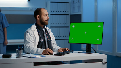 Physician medic working late at night on computer with green screen template checking patient report planning medication treatment to help curse disease in hospital office. Health care service