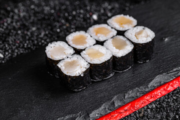 Asian cuisine. Roll with scallop on a black stone on a black background. rice nori scallop