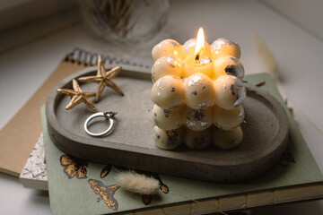 A square bubble candle is burning on a concrete stand. 