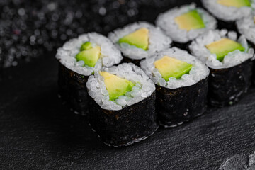Asian cuisine. Roll with avocado on a black stone on a black background. rice nori avocado