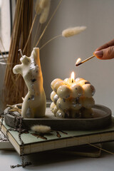 A bubble candle and a white candle shaped as a female body on a concrete tray. Woman lights the candle