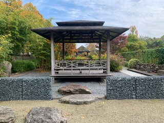 Japanese tea gazebo on a wooden platform in the autumn garden. Gabions and boulders on a flat area of fine gravel. Appeltern, Netherlands, October 12, 2022