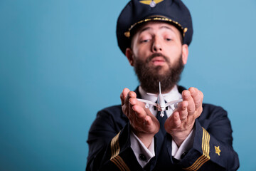 Airplane captain in uniform holding plane model in palms front view, pilot playing with commercial passenger jet toy. Professional aviation academy aviator on blue background