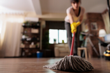 Housemaid cleaning floor with mop wearing cleaning gloves, finishing cleaning apartment for client....