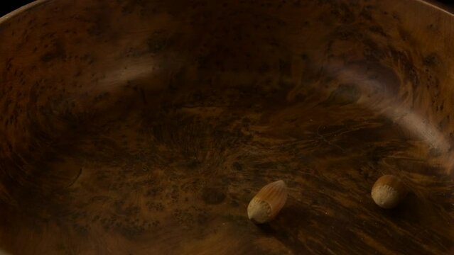View from above of a wooden bowl in rotation with hazelnuts falling