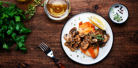 Fried chicken breast fillet with champignon mushrooms and onion in white wine sauce with thyme on plate, rustic wooden table background, top view