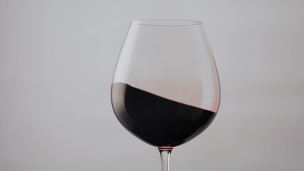 Red wine wave glass goblet on white background close up. Drink swirling inside.