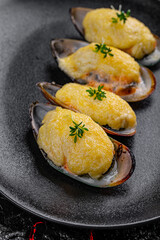 Asian cuisine. Oysters baked with cheese in a black plate on a black background.