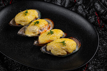 Asian cuisine. Oysters baked with cheese in a black plate on a black background.