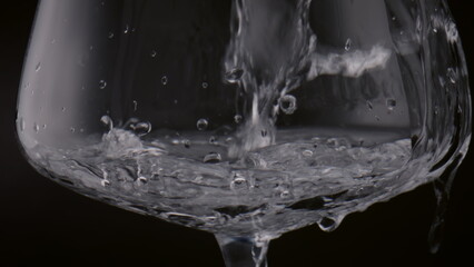 Clean water splashing goblet on black background closeup. Drink pouring in glass