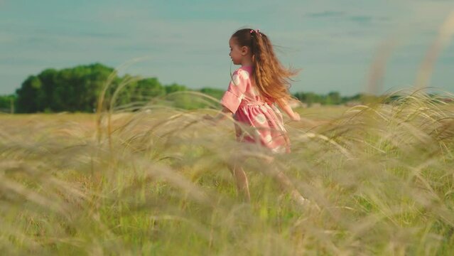 Little girl runs on grass, in sun, slow motion. Happy family concept, childs dream. Kid runs across meadow. Childhood dream. Happy little girl playing at sunset. Happy child in field at sunset