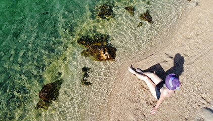 Eine Frau mit Badeanzug und Strohhut sitzt im Sand am Meer