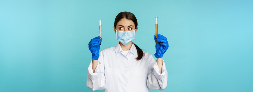 Image Of Young Woman Doctor, Lab Worker Doing Research, Holding Test Tubes, Wearing Medical Face Mask And Rubber Gloves, Blue Background