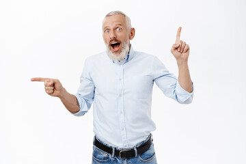 Portrait of senior business man pointing up and left, showing two promos, standing in blue shirt and jeans over white background