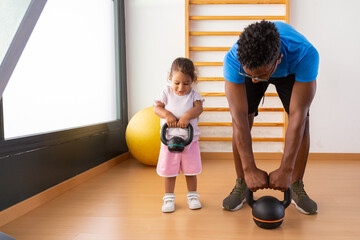 Little kid lifting kettlebell with father	 