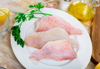 Raw rockfish fillet on plate, garlic, parsley and salt on wooden table. Ingredients for cooking