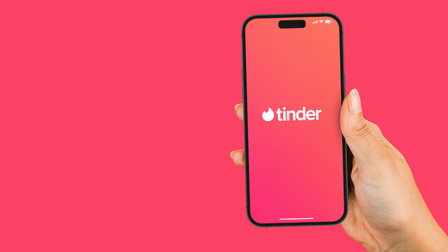 Female hand holding a smartphone iPhone 14 Pro with Tinder app on the screen. Pink background. Rio de Janeiro, RJ, Brazil. November 2022