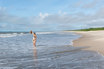 An adult woman in a bikini walking under strong sunlight on beach