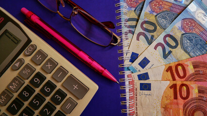  Euro with calculator, pen and glasses on the purple notebook.