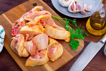 Fresh raw chopped chicken pieces on a wooden cutting board with a sprig of fresh parsley, garlic and vegetable oil during ..cooking in a home kitchen