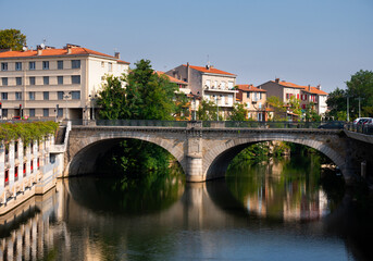 Fototapeta na wymiar Scenic view of summer townscape of Castres with modern townhouses with terracotta tiled roofs on bank of Agout river and old Pont Miredames arched bridge on sunny day, France