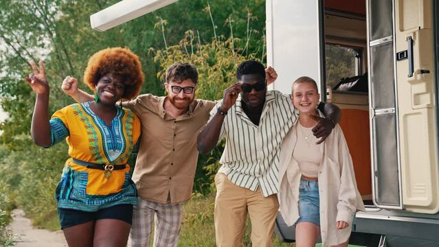 Diverse group of young adult friends standing outside camper van in field embracing each other posing for picture smiling. Horizontal outdoor video. High quality 4k footage