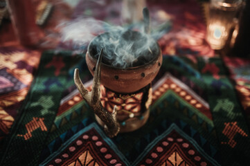 Smoking incense burner with coal on a colorful blanket with indigenous pattern at spiritual...