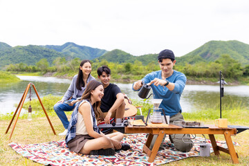 Group of Asian people enjoy and fun outdoor lifestyle hiking and camping together on summer travel vacation. Man and woman friends having breakfast drinking brewed coffee near the tent in the morning.