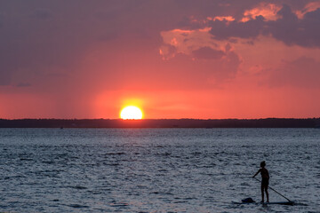 A woman rides a stand-up paddleboard at sunset