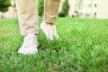 Man in stylish sneakers walking on green grass outdoors, closeup
