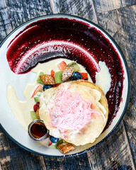A serving of stacked pancakes with raspberry sauce, fruit pieces and pink fairy floss