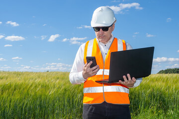 Foreman construction companies. Man with laptop and phone in hands. Foreman is standing in wheat...