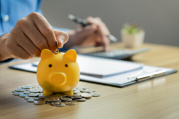 Businessman calculates savings on his desk and piggy bank and piles of coins. investment and...