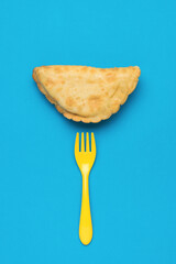 Yellow fork and fresh cheburek on a blue background.