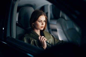 Fototapeta na wymiar a sweet, relaxed, stylish woman is sitting in a black car in the passenger seat, at night and wearing a seat belt. Topics of road safety