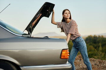 The woman driver of the car opened the trunk with looks. Car breakdown while traveling on the road. Car and woman repair concept