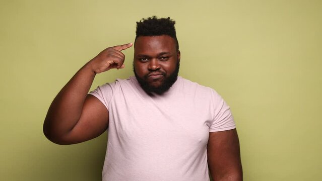 Crazy idea. African-american man showing stupid gesture, looking at camera with condemnation and blaming for insane plan, dumb suggestion. Indoor studio shot isolated on light green background.