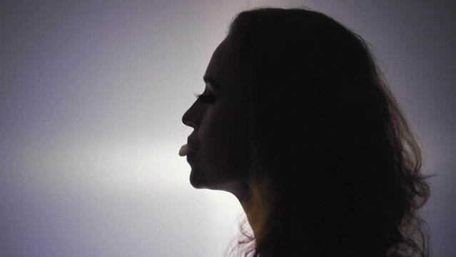 Female profile with gumball. Silhouette shooting against on a gradient background. The cute girl pouting a ball of chewing gum and bursting it waving long eyelashes 