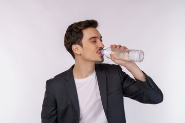 Portrait of Happy young man drinking water from a bottle and looking at camera isolated over white background
