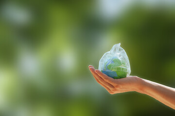 Zero waste. hand holding the earth that plastic bag covering on a green background. Concept of...
