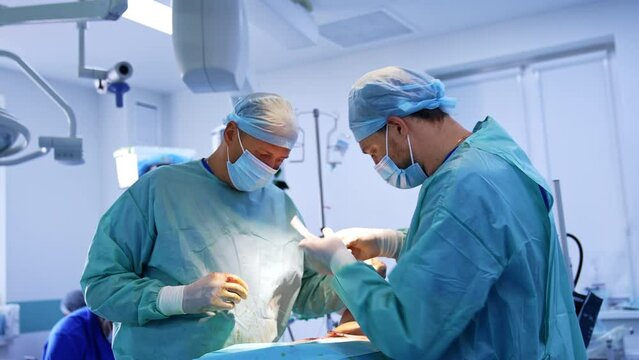Plastic surgery professionals performing abdominal surgery. Doctors sew the patient's cut using the forceps and threads.