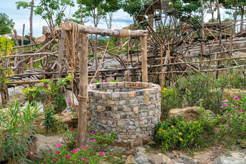 Beautiful artesian well made by bricks with cement and wheel pulley with metal bucket and rope in peaceful garden atmosphere. Retro stone water well in rural area.Garden decoration with antique items