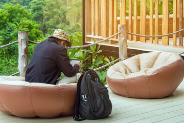 Male tourist wear hat with face mask with backpack use tablet while sit to relax on large cushions...