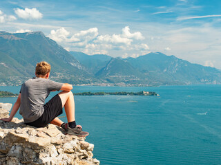Teenager with sports body resting on rough stony wall above lake