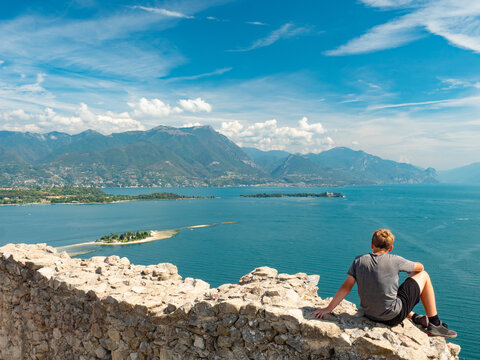 Boy sit  alone on rest of Manerba castle wall above Lago di Garda lake