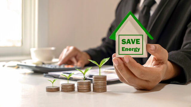 Businessman Holding Greenhouse Model For Saving Energy And Trees Growing On A Pile Of Mortgage Ideas. Real Estate Business Loan