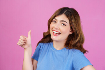 Portrait of happy young woman wearing casual t-shirt showing thumb up isolated over pink background