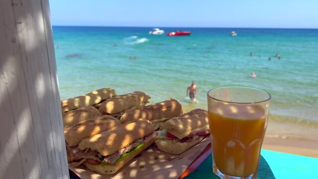 Delicious sandwiches at a beautiful beach bar with fresh orange juice, enjoying summer with dreamy holiday sea view in Ibiza Spain, vacation destination, 4K shot